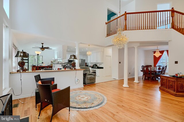 dining area with ornate columns, a chandelier, a ceiling fan, light wood-style floors, and a high ceiling