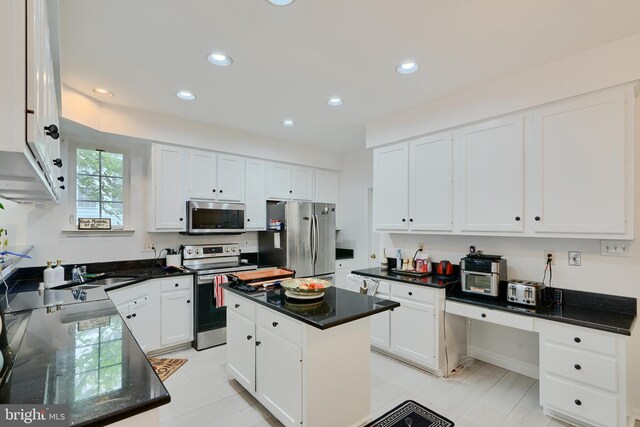 kitchen with stainless steel appliances, white cabinetry, a sink, recessed lighting, and dark stone countertops