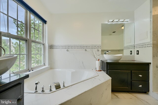 bathroom featuring healthy amount of natural light, a garden tub, marble finish floors, and vanity