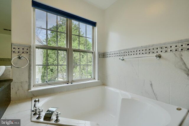 full bathroom featuring healthy amount of natural light, a bath, and tile walls