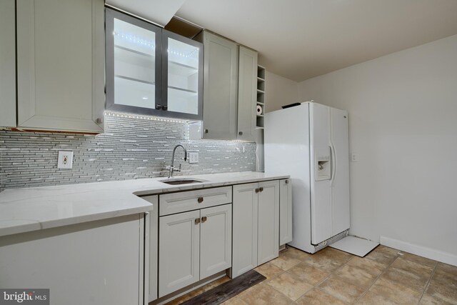 kitchen with a sink, decorative backsplash, white fridge with ice dispenser, light stone countertops, and open shelves