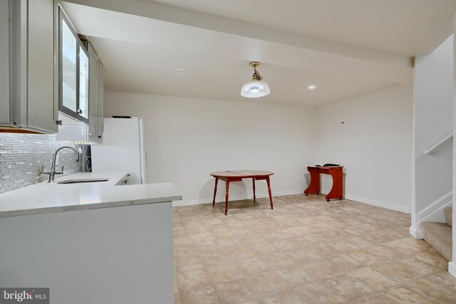 kitchen featuring a sink, light countertops, tasteful backsplash, freestanding refrigerator, and hanging light fixtures