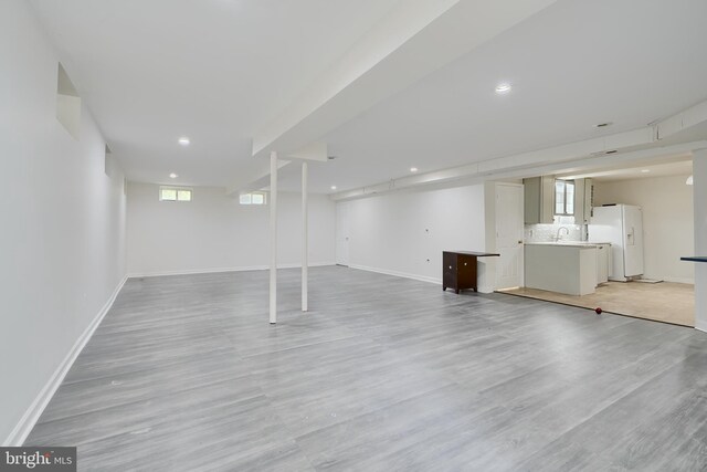 below grade area with white refrigerator with ice dispenser, baseboards, light wood-type flooring, and recessed lighting