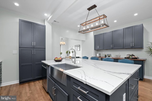 kitchen with a sink, light stone countertops, wood finished floors, recessed lighting, and stainless steel dishwasher