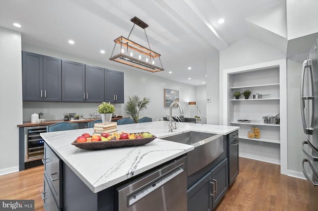 kitchen with stainless steel appliances, a sink, beverage cooler, an island with sink, and light stone countertops