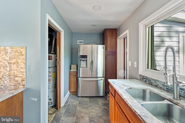 kitchen with stainless steel fridge, a sink, brown cabinetry, and gas water heater