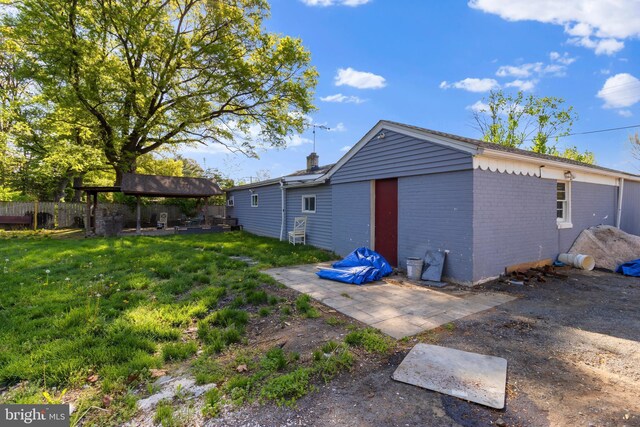 rear view of house featuring a chimney, a lawn, brick siding, fence, and a patio