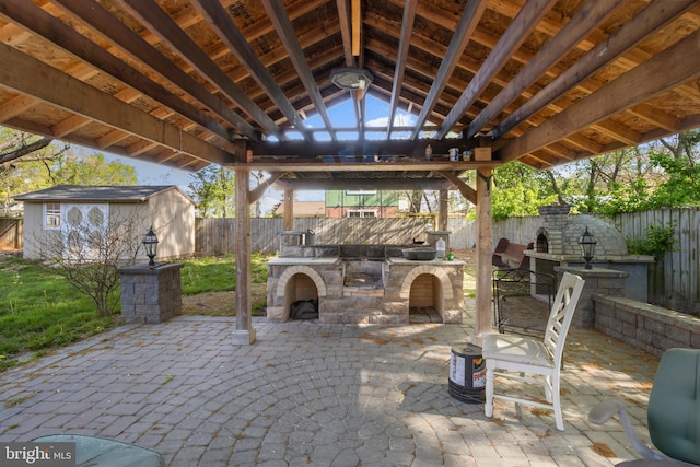 view of patio / terrace with a fenced backyard, an outbuilding, a gazebo, and an outdoor stone fireplace