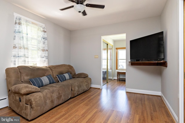 living area featuring baseboards, a ceiling fan, a baseboard heating unit, and wood finished floors