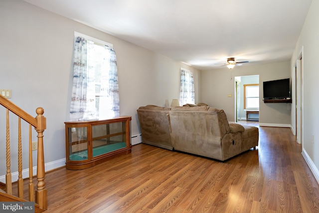 living room with stairs, a ceiling fan, baseboards, wood finished floors, and a baseboard radiator
