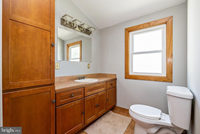 bathroom featuring tile patterned flooring, vanity, toilet, baseboards, and lofted ceiling