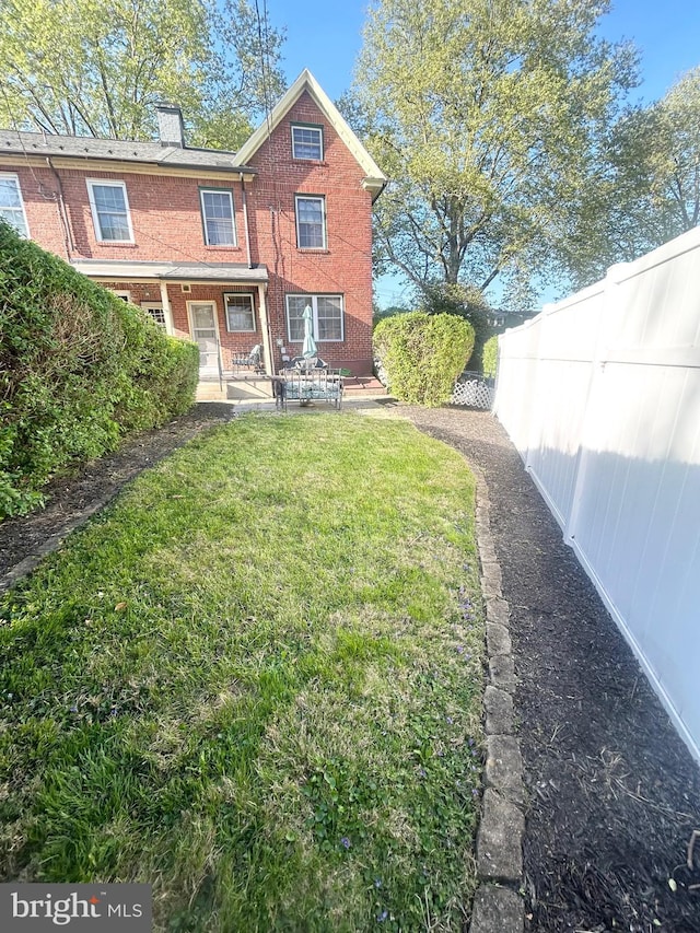 back of property featuring a yard, brick siding, fence, and a chimney