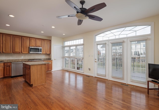 kitchen with brown cabinetry, visible vents, dark wood-style floors, a center island, and appliances with stainless steel finishes
