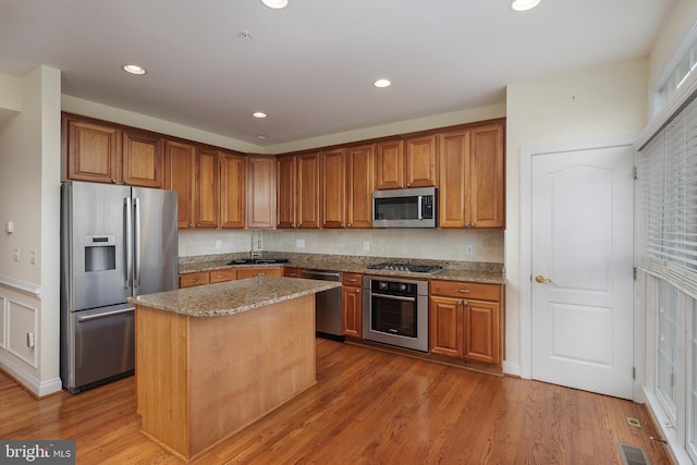 kitchen featuring visible vents, a kitchen island, light stone countertops, a sink, and stainless steel appliances