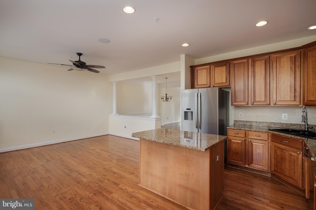 kitchen featuring a kitchen island, stainless steel refrigerator with ice dispenser, brown cabinets, a sink, and stone countertops