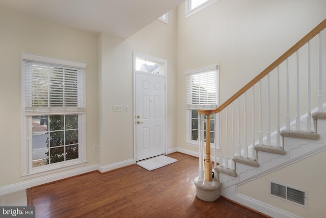 foyer with a towering ceiling, stairs, wood finished floors, and visible vents