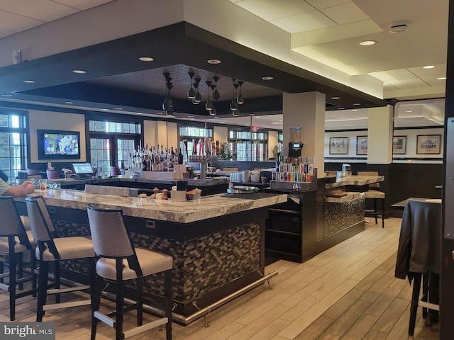 bar with a healthy amount of sunlight, a raised ceiling, indoor wet bar, and light wood-type flooring