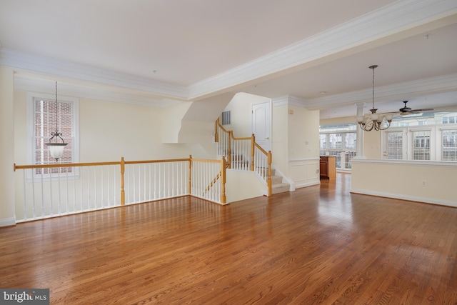 unfurnished living room with stairway, ornamental molding, ceiling fan with notable chandelier, and wood finished floors