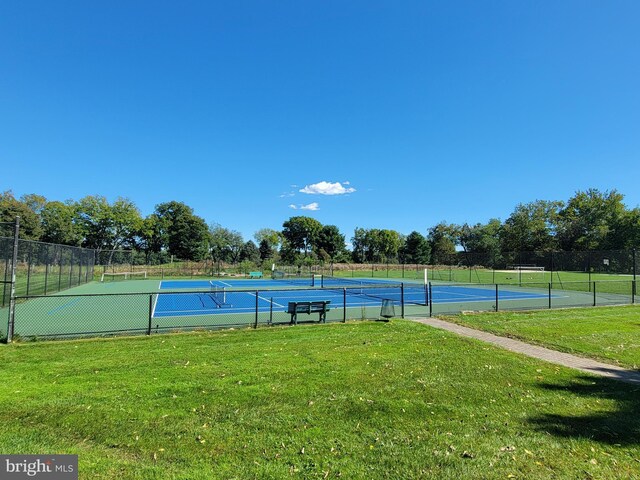 view of tennis court with a yard and fence