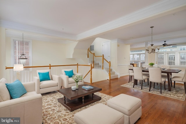 living area with ornamental molding, ceiling fan with notable chandelier, stairs, and wood finished floors