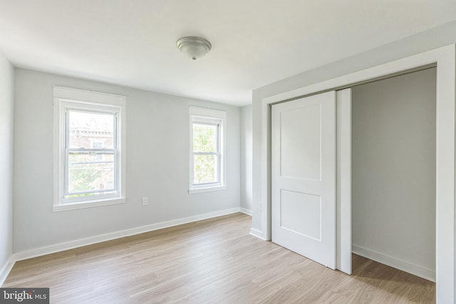 unfurnished bedroom featuring light wood-type flooring, baseboards, and a closet