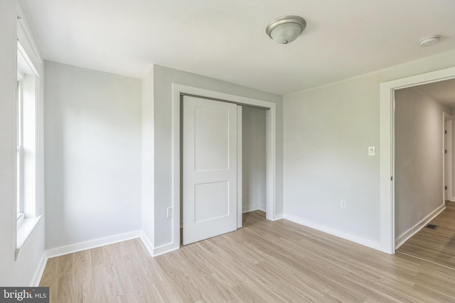 unfurnished bedroom featuring baseboards, light wood-style flooring, and a closet