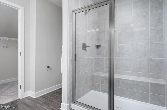 bathroom featuring baseboards, a shower stall, wood finished floors, and a walk in closet