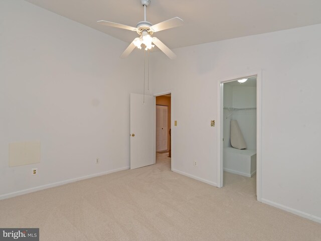unfurnished bedroom with a walk in closet, ceiling fan, baseboards, a closet, and light carpet