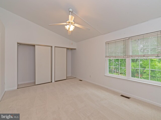 unfurnished bedroom featuring visible vents, two closets, baseboards, light colored carpet, and vaulted ceiling