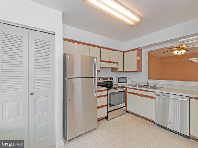kitchen featuring light countertops, a sink, under cabinet range hood, light floors, and stainless steel appliances