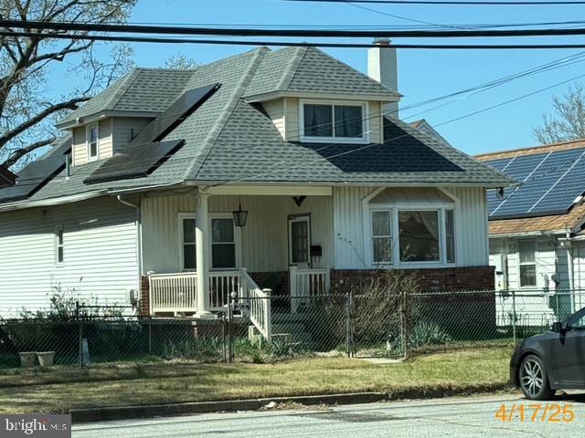 view of front of home featuring roof with shingles, a fenced front yard, brick siding, a porch, and a chimney