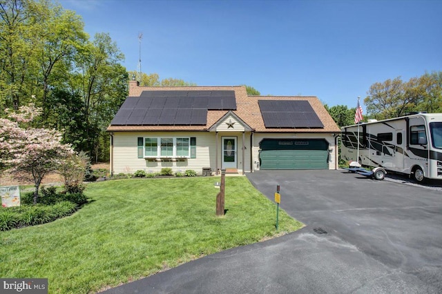 view of front facade with driveway, a chimney, solar panels, a front lawn, and an attached garage