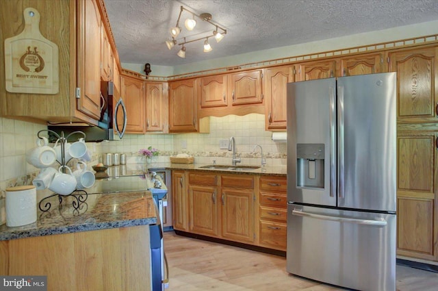 kitchen featuring decorative backsplash, a sink, stone countertops, light wood-style floors, and stainless steel appliances