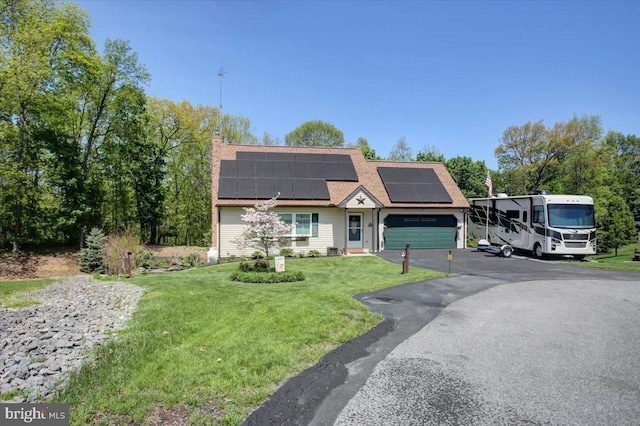 colonial inspired home featuring a front lawn, aphalt driveway, a garage, roof mounted solar panels, and a chimney