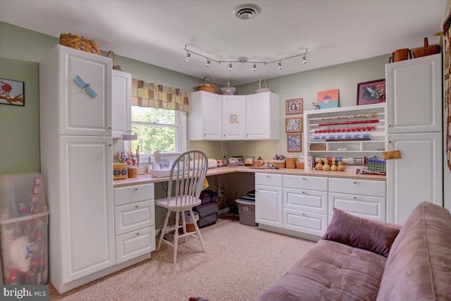 home office featuring built in study area, visible vents, and light colored carpet