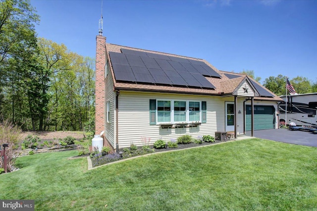 view of front facade featuring an attached garage, a front yard, a chimney, solar panels, and driveway