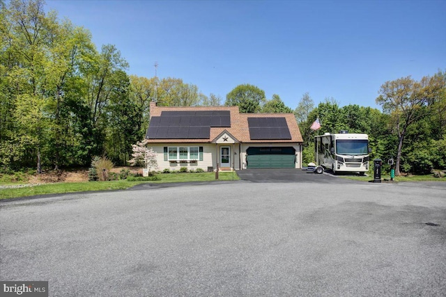 colonial inspired home featuring roof with shingles, an attached garage, solar panels, and aphalt driveway
