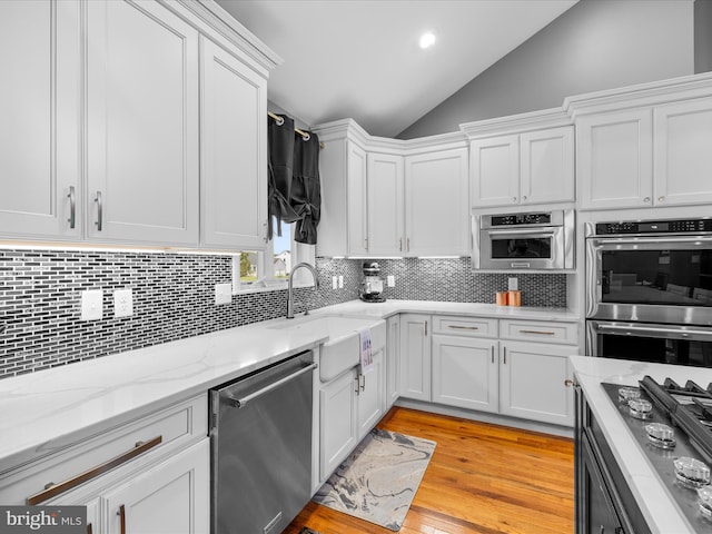 13295 Rollie Road E Rd, Bishopville, MD 21813 - kitchen with appliances with stainless steel finishes, vaulted ceiling, white cabinets, backsplash, and light wood-style flooring