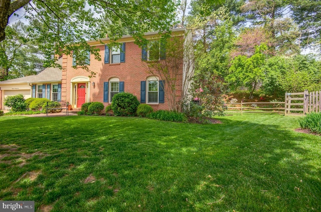 colonial home with fence, a garage, brick siding, and a front yard