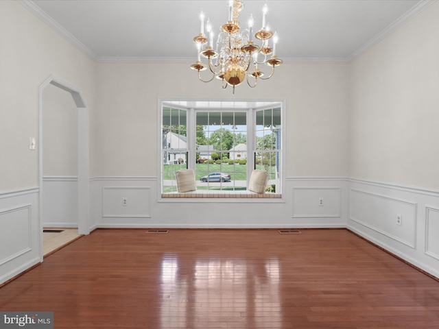 unfurnished dining area featuring crown molding, a notable chandelier, wainscoting, wood finished floors, and visible vents