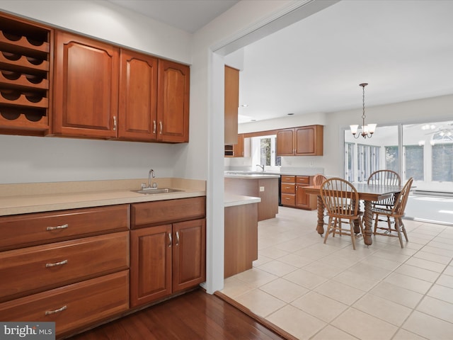 kitchen with brown cabinets, hanging light fixtures, an inviting chandelier, a sink, and light countertops