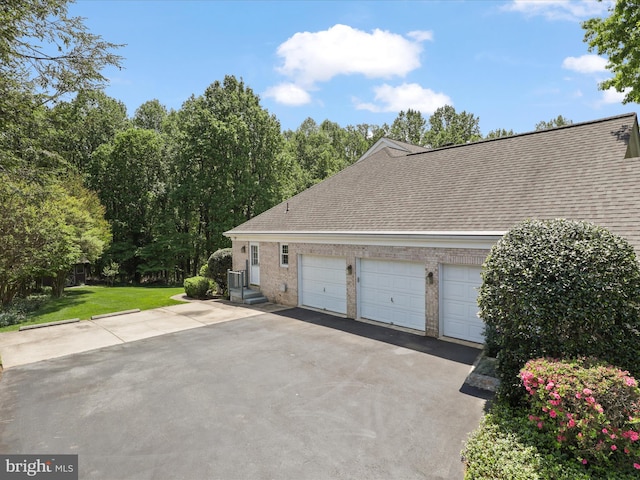 view of side of property with driveway, a lawn, brick siding, an attached garage, and a shingled roof