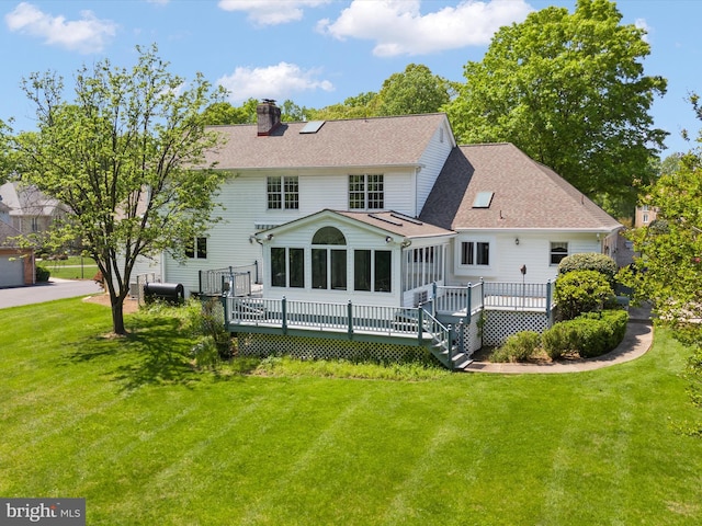 back of property featuring a chimney, a sunroom, a yard, and a deck