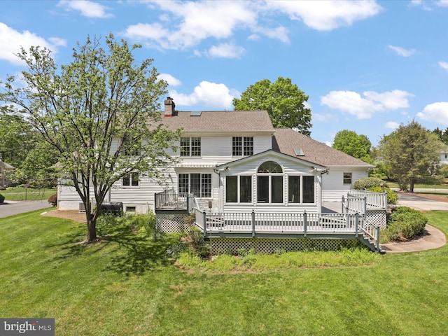 back of property featuring a yard, a deck, a chimney, and a sunroom