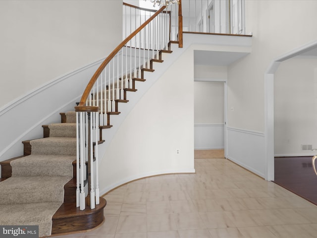 stairs featuring visible vents, arched walkways, baseboards, and a high ceiling