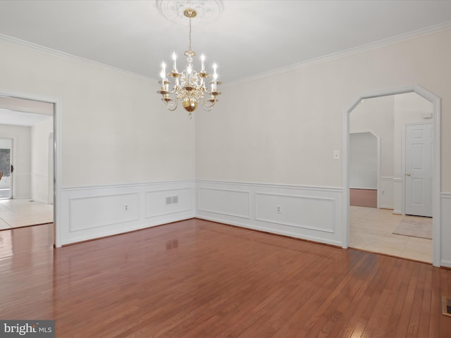 empty room featuring an inviting chandelier, ornamental molding, wainscoting, and hardwood / wood-style floors