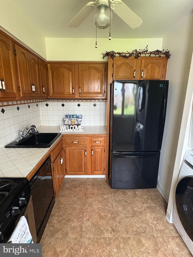 kitchen featuring tile countertops, brown cabinets, a sink, backsplash, and black appliances