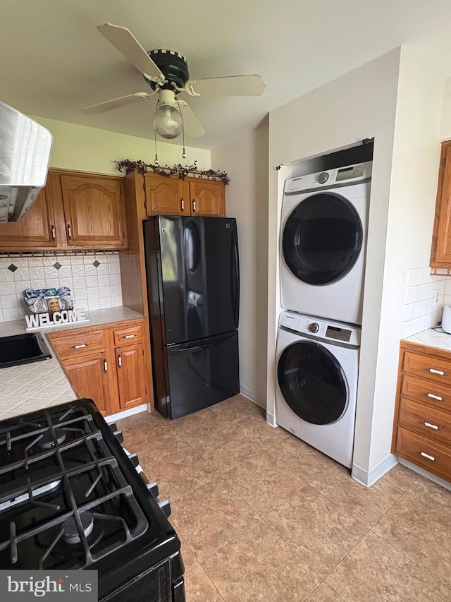 kitchen with tasteful backsplash, brown cabinets, stacked washing maching and dryer, black appliances, and tile counters