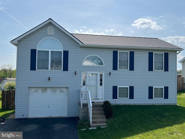 raised ranch with an attached garage, fence, a front yard, and aphalt driveway