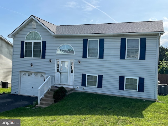 bi-level home featuring an attached garage, central AC unit, a front lawn, and aphalt driveway
